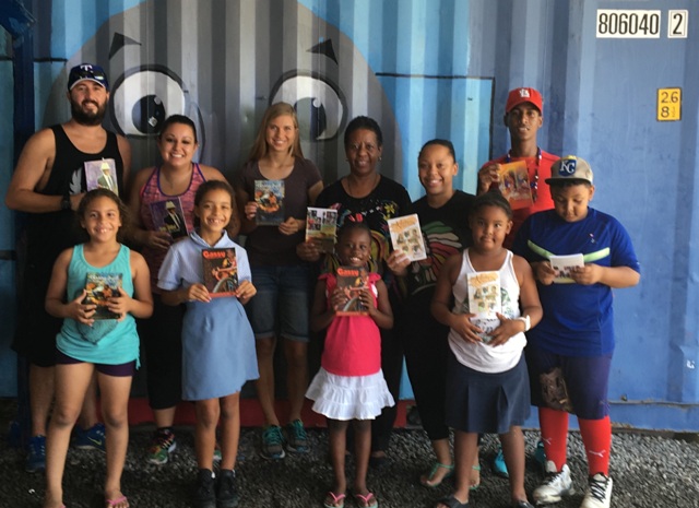 Caption: Player Development SXM kids with jr. scholastic booklets and books published in St. Martin. Among the community-minded adults in back row: AUC volunteer Jay Webb (L) and educator Carmen Bowers (4th L), who presented the books on behalf of HNP. (Courtesy photo)